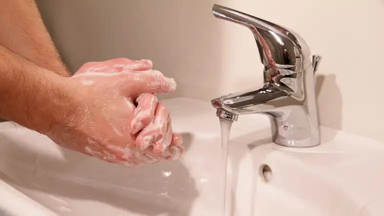 en person vasker hænder under vandhanen