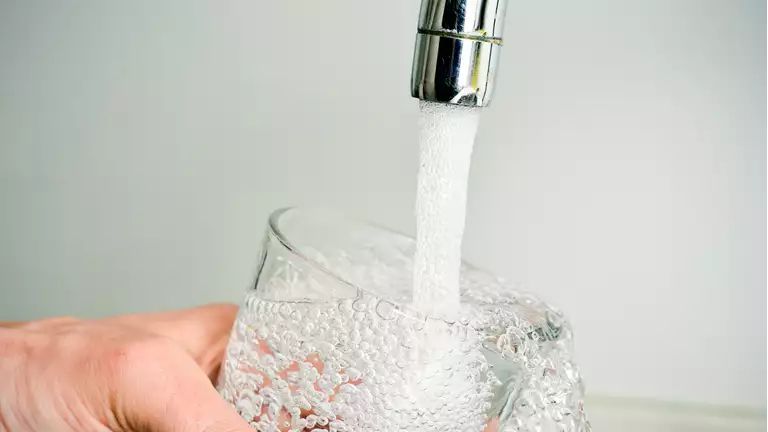 en person fylder et glas med vand fra vandhanen
